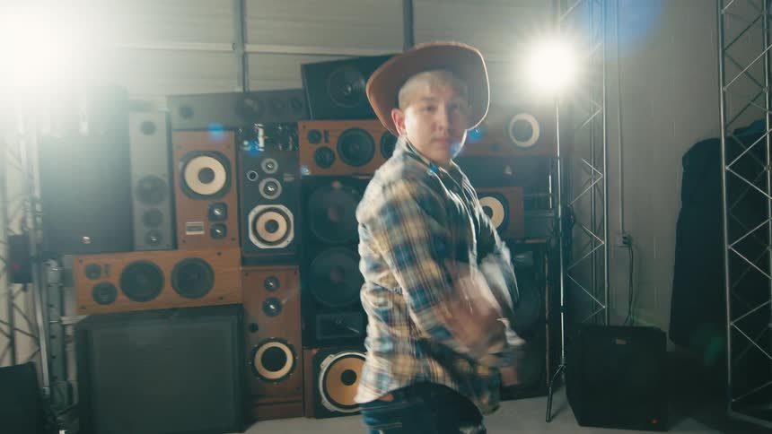 A man dances in a studio in front of several stacked speakers under scaffolding