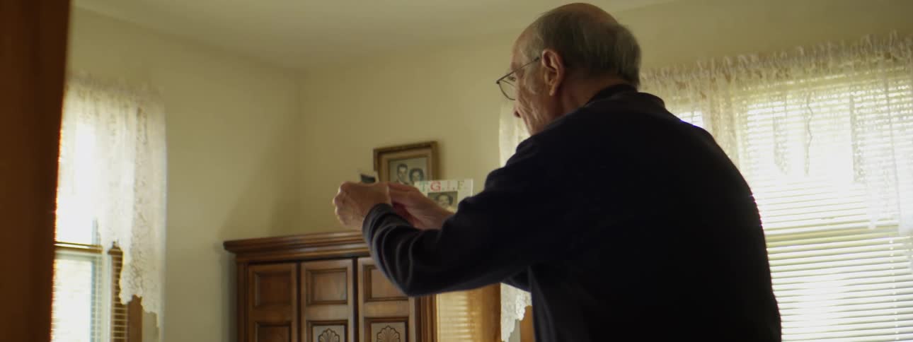 A man in a bedroom holding a projector slide with walls and windows in the background