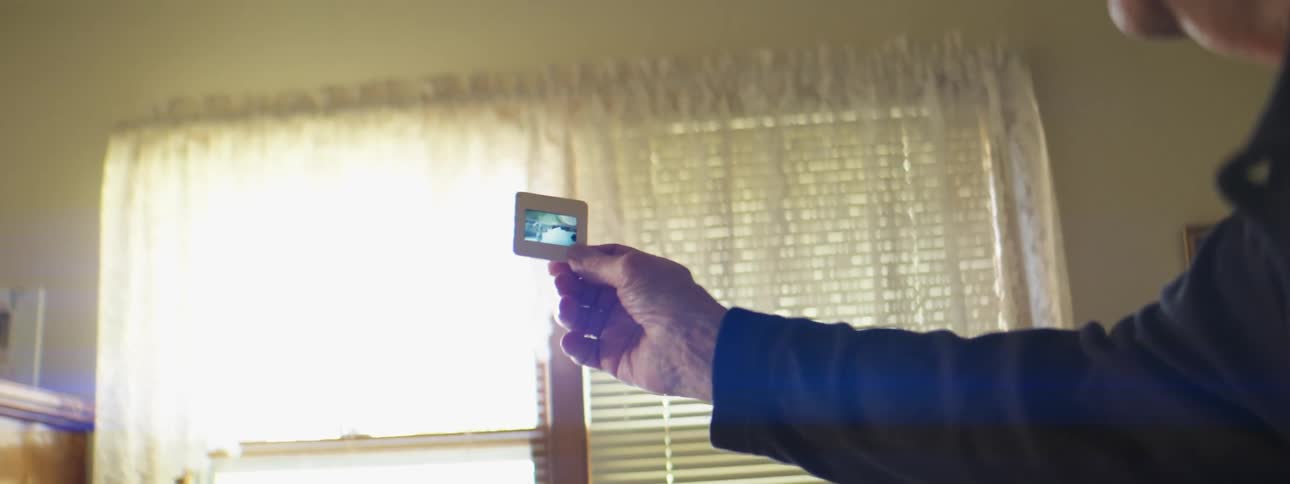 A person in a room holding up a projector slide with a wall and window in the background