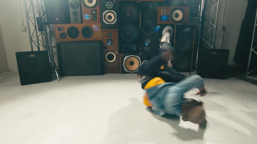A man is break dancing in front of a stack of speakers