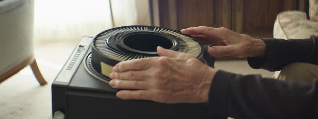 Elderly man sitting in living room sets up slide projector
