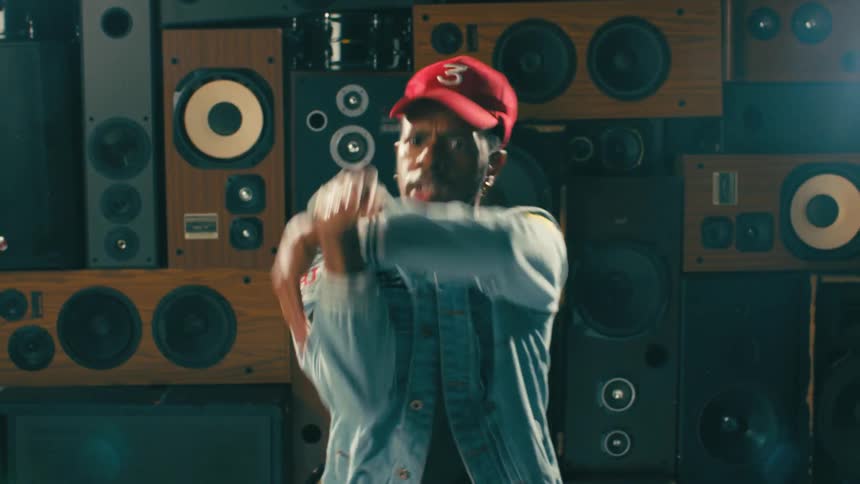 A man performs a series of robotic dance moves while hes in front of a stack of stereo speakers