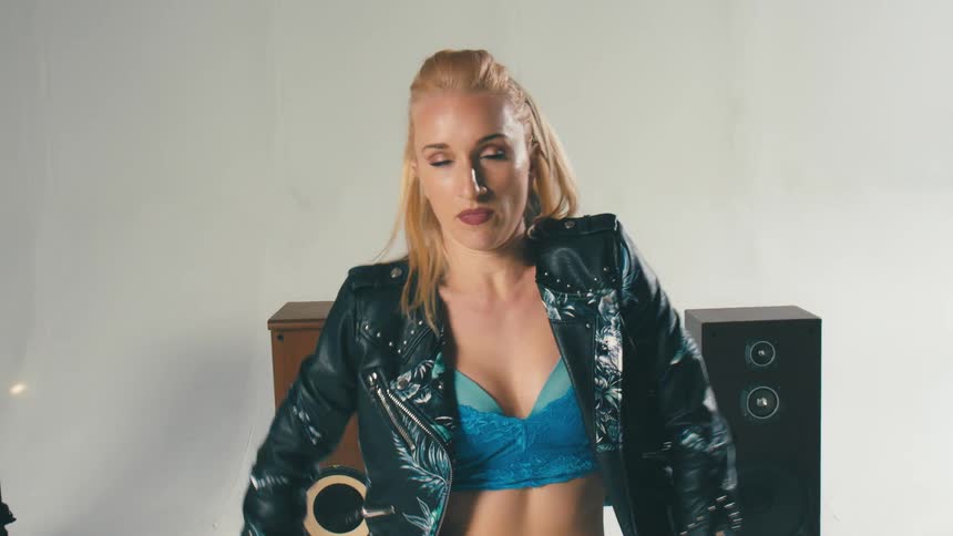 A woman in a leather jacket and ripped jeans dancing in front of large speakers
