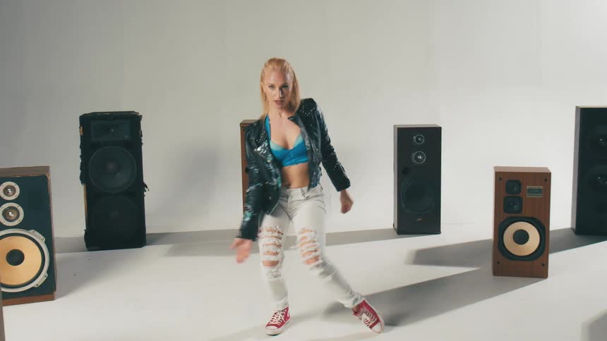 Young blonde woman energetically dancing inside a circle of speakers