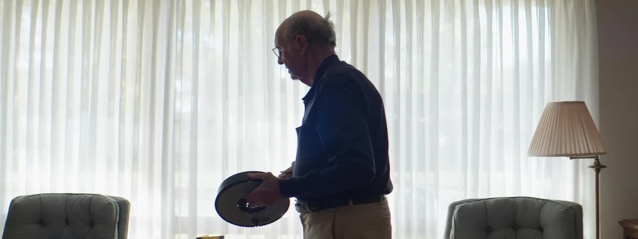 A man stands in front of his large window holding up a slide from a slide wheel