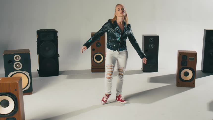 A woman wearing casual clothing does a pirouette in a room filled with speakers