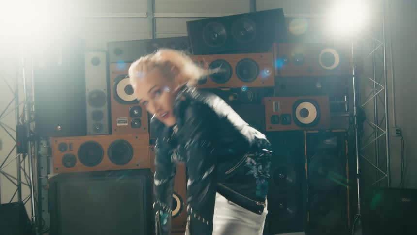 Young blonde woman energetically dancing in front of a tower of speakers