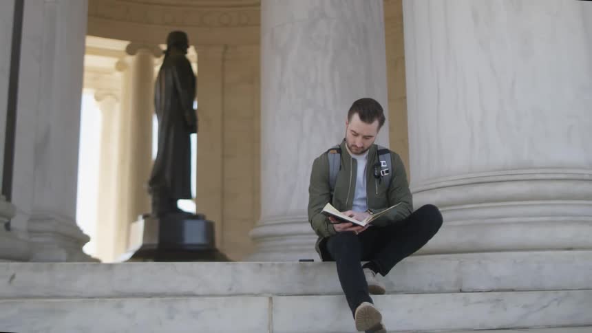 A man sits and flips through a notebook on the marble steps of the Thomas Jefferson Monument