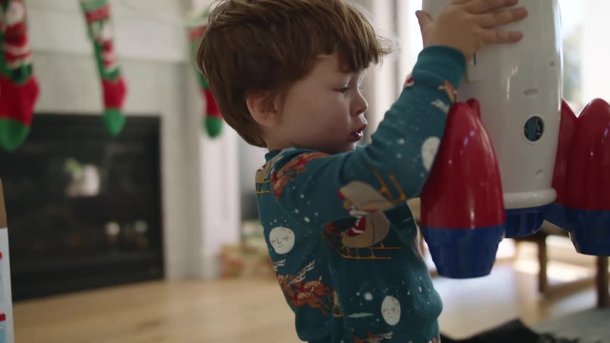 A little boy lifts up a rocket toy on a bright sunny christmas morning