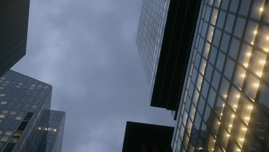 City buildings with glowing window lights and the glare of a street light against a cloudy sky