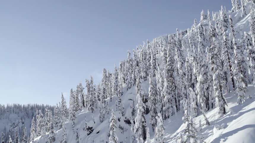 Skimming low along the incline of a steep and snowy mountain under a bright blue sky