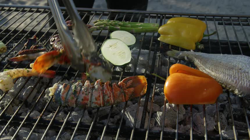 A man flips over a lobster on an outdoor charcoal grill at the beach