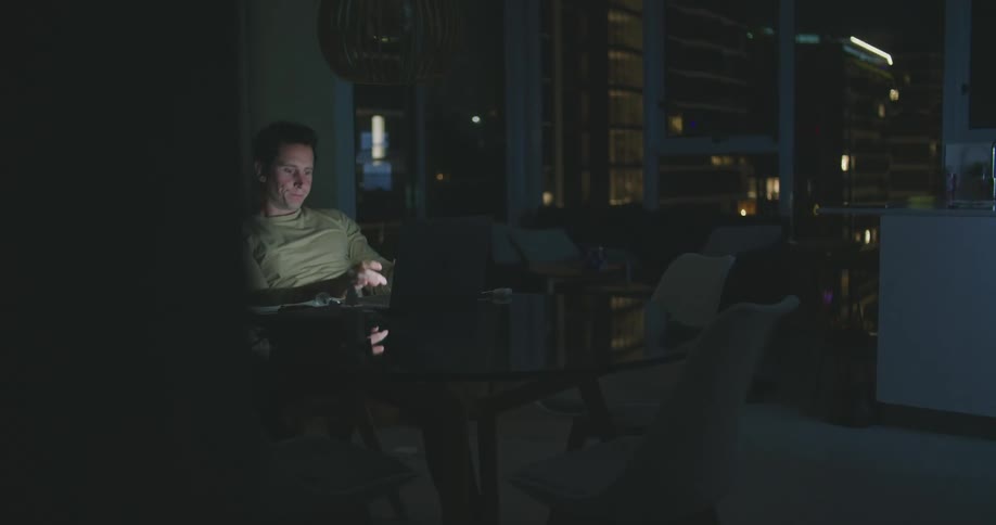 A man is sitting in a room looking at a laptop