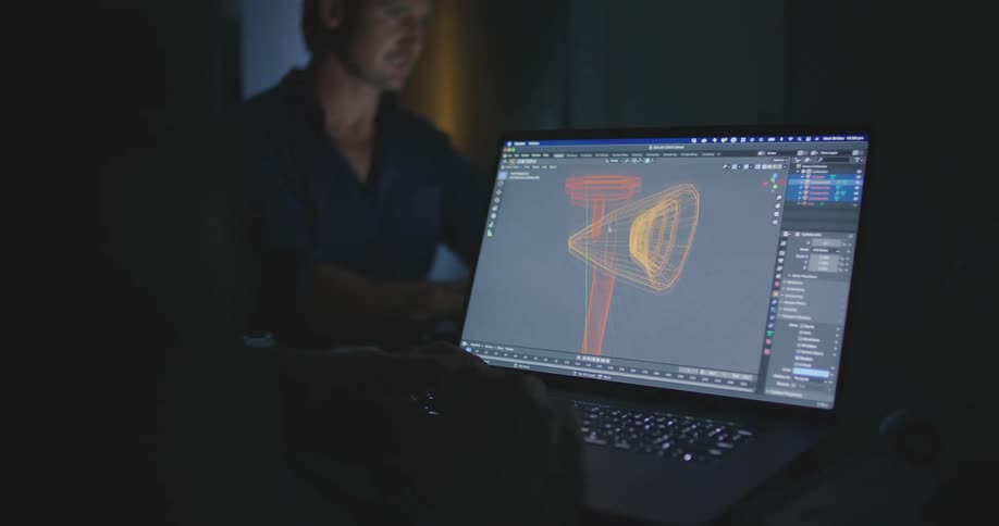 A person sitting in front of a laptop computer works on a graphic design indoors at nighttime