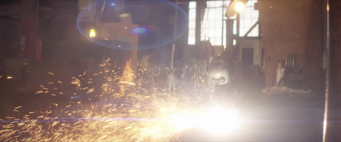 A person with a welding helmet welding with sparks with a wall and window in the background
