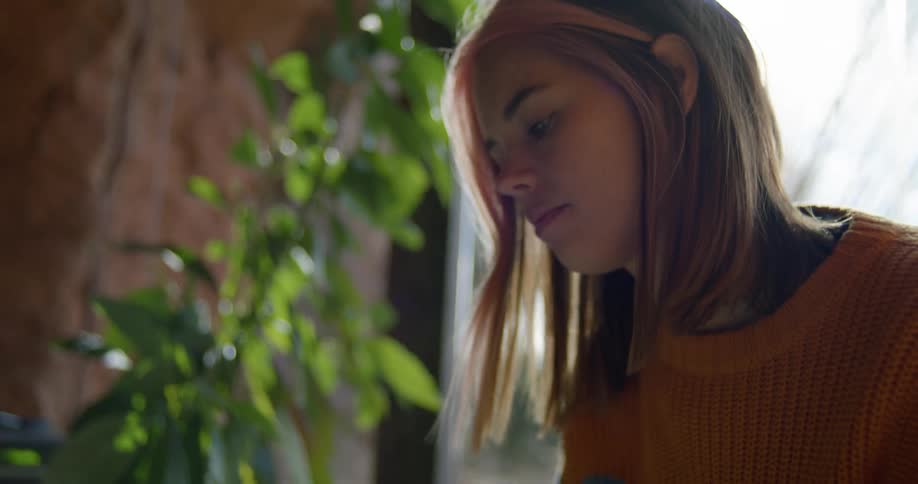 A woman in a room looking at a book with a plant and a wall in the background