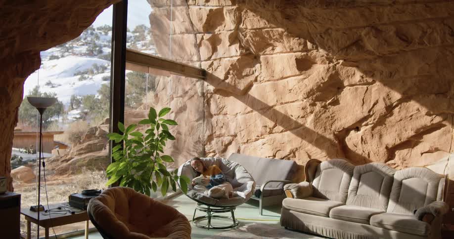 Woman reads while sitting in living room situated in cavern with view of snow covered slope