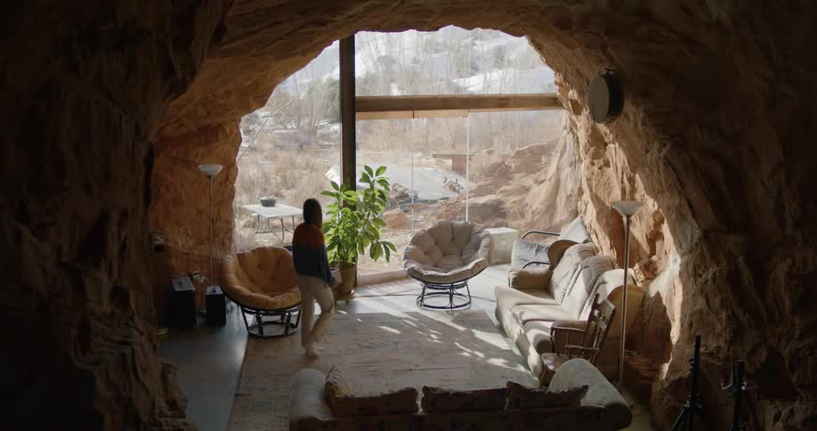 A woman walks around a living room and looks out the window