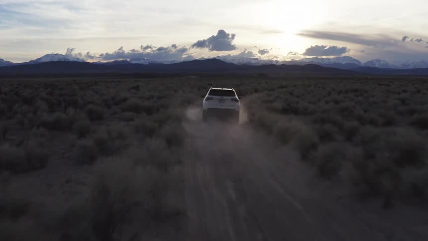 Suv drives along dirt road through scrub plain toward mountains kicking up dust