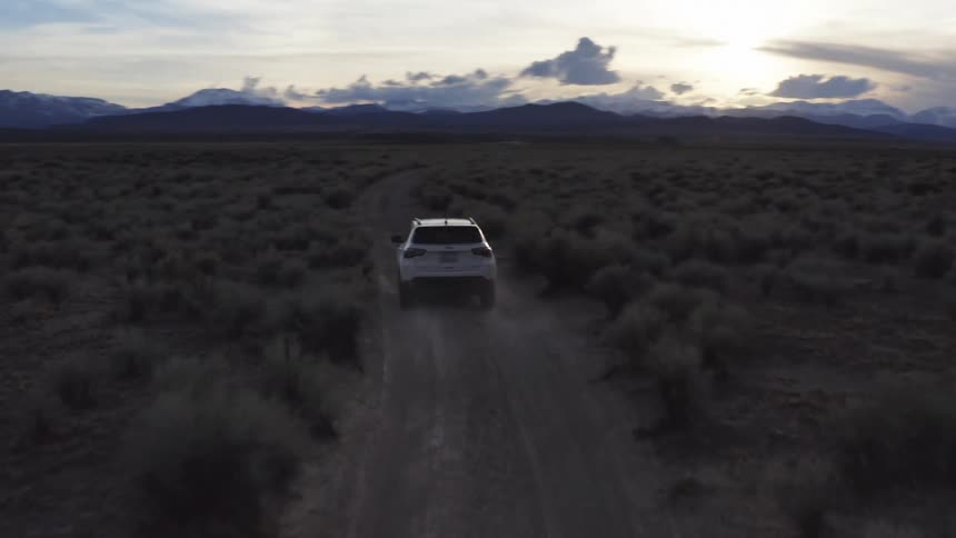 A vehicle driving in a desert dirt road with a mountain range the sky and clouds in the background