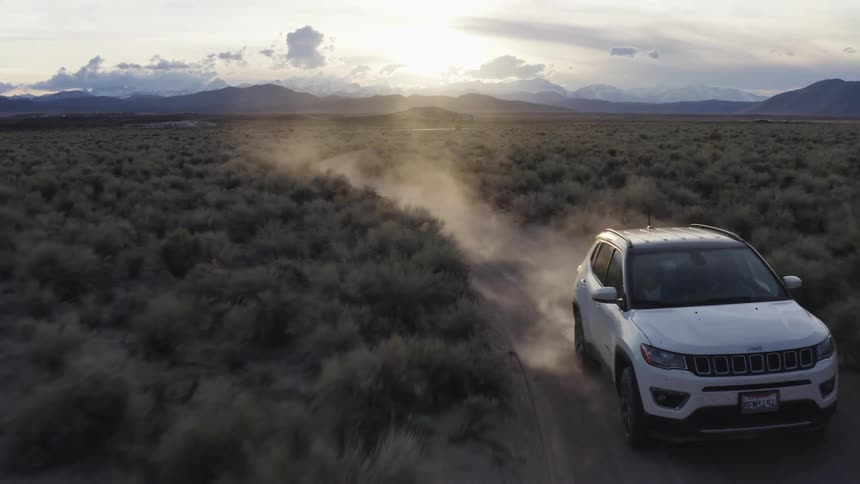 A person with a passenger drives a vehicle down a dirt road in the middle of a grassland