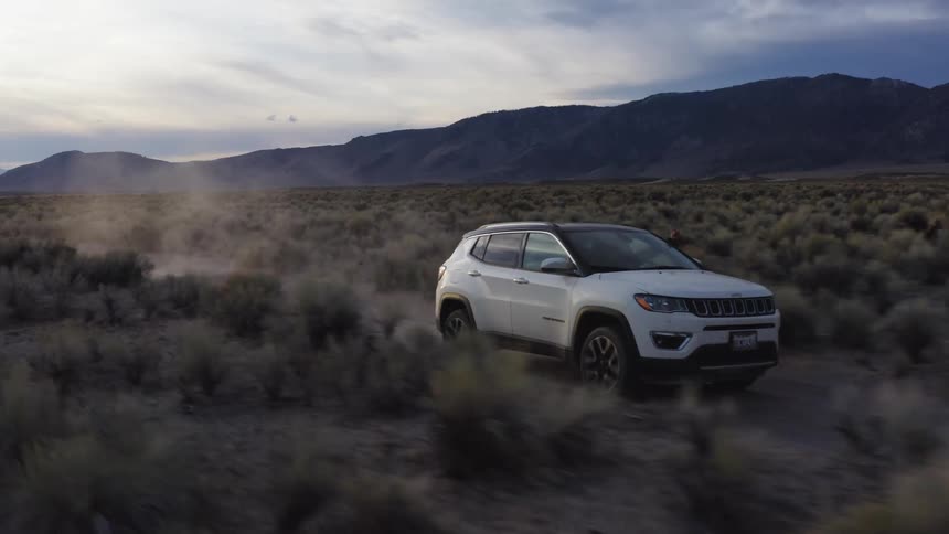 Vehicle drives through scrub with mountains on the horizon kicking up dust