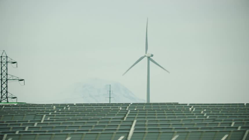 Wind turbine spinning behind a row of solar panels that eventually reveal high tension transmission lines in this visual energy shot