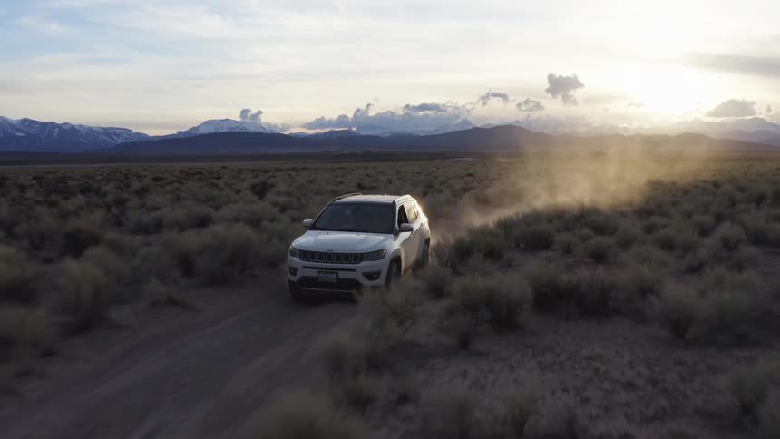 A vehicle driving in a desert dirt road with a mountain range the sky and clouds in the background