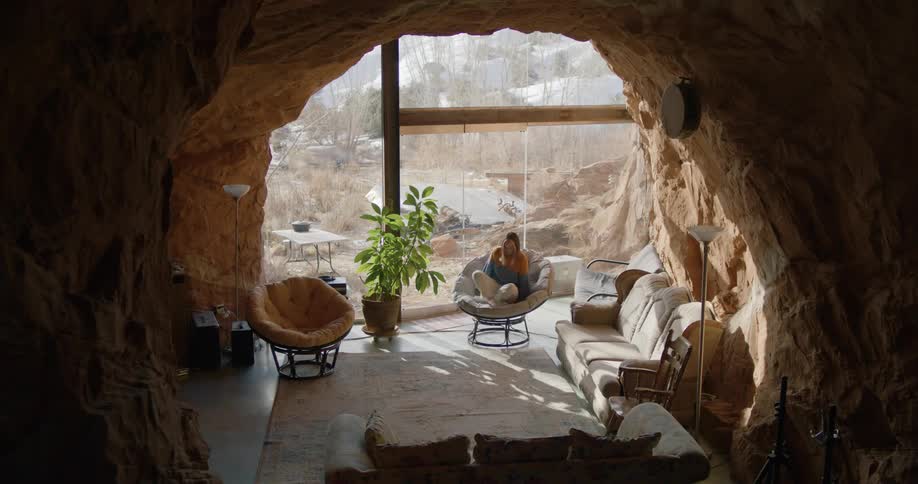 Woman wearing a sweater sits on a chair inside a room built inside a cave