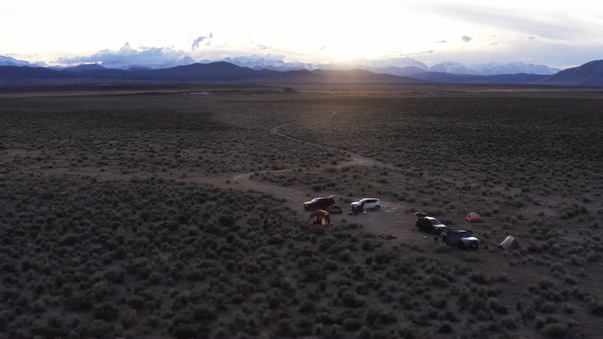 A desert with people tents and vehicles with a mountain range the sky and clouds in the background