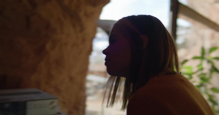 A woman looks around a living room with rock cave walls and a sunny glass front