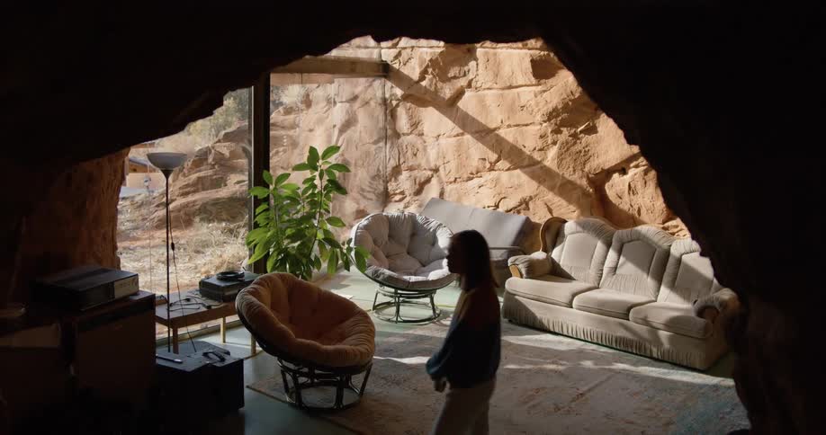 A woman walks through a room with rock walls and a glass front