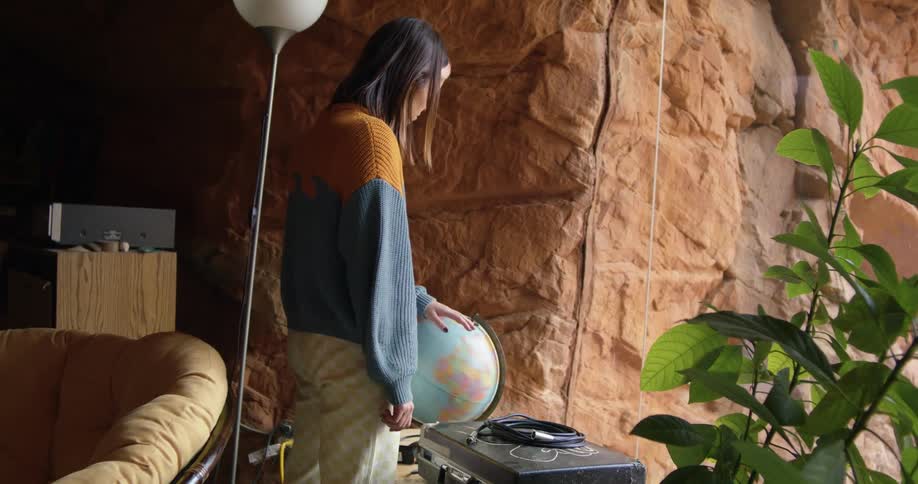 Woman wearing sweater stands in living room with natural cavern walls spinning a globe