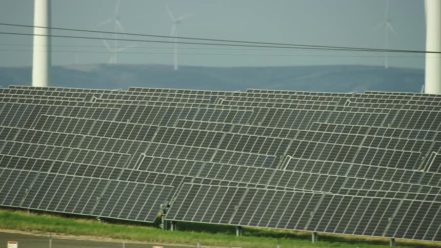 A solar farm in the foreground as wind turbines spin in the background as two renewable power generators are pictured in the same frame