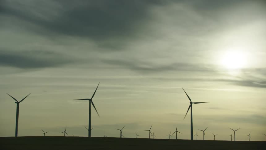 Silhouetted wind turbines against a golden backlit sky generate wind energy in a renewable form in this late afternoon shot