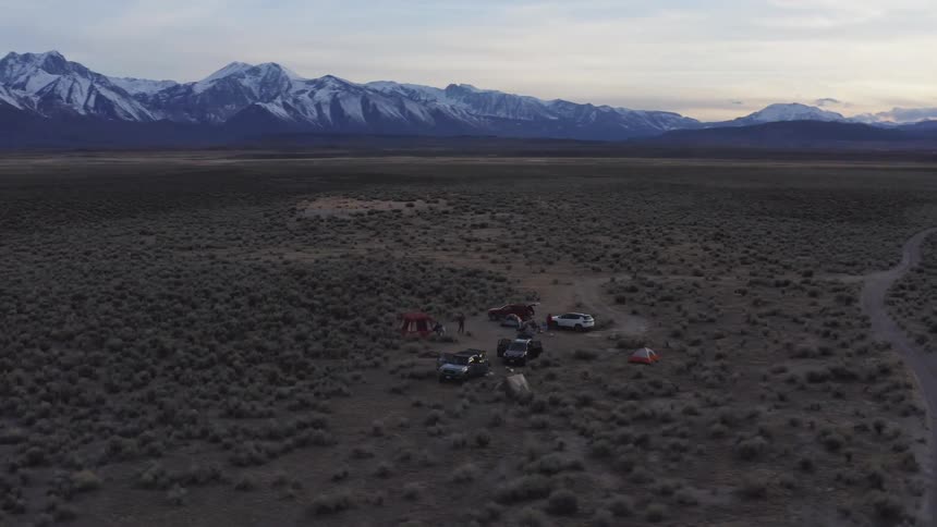Cars and tents create a campsite off road with mountains and lake on the horizon