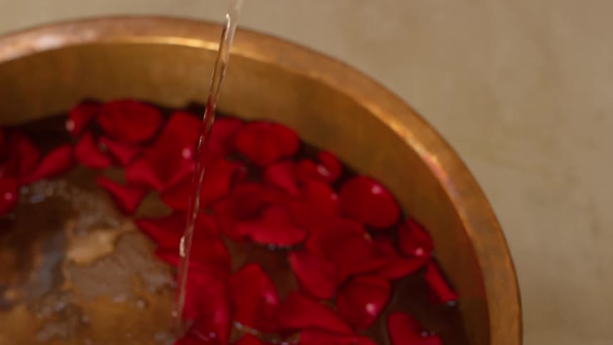 A faucet filling a basin with rose petals and water