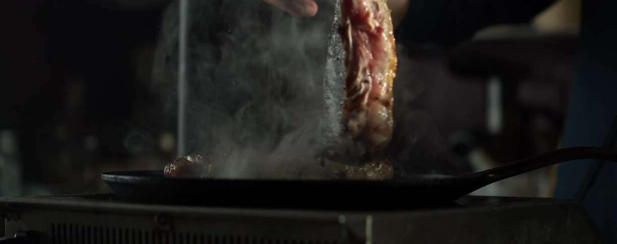 Person turns large piece of meat on smoking grill