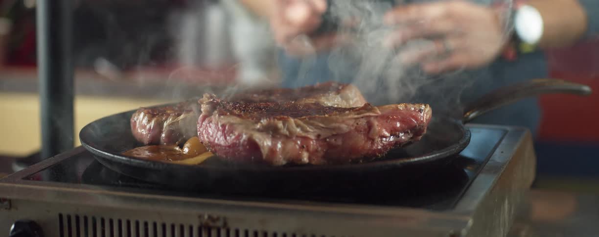 Man cooking beef steaks over a frying pan in the kitchen