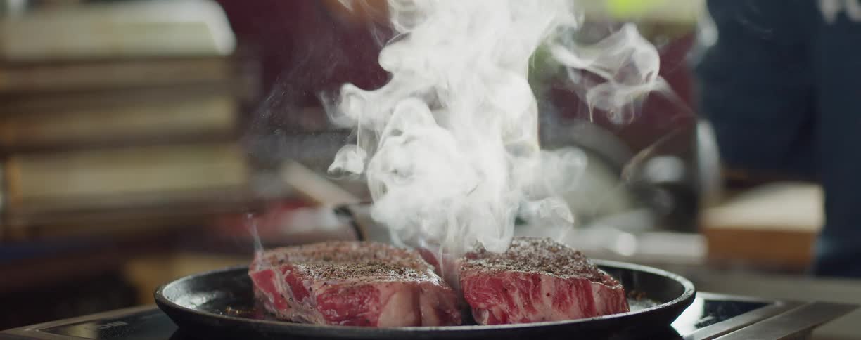 A person stands behind steaks cooking on a pan at home