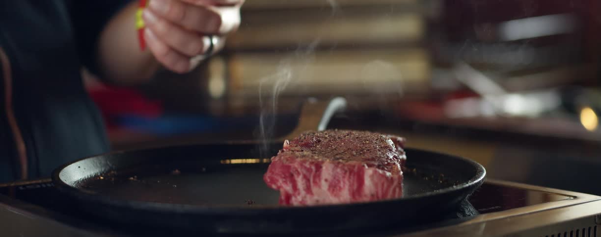 A person places a steak on a hot skillet lying atop an induction cooktop