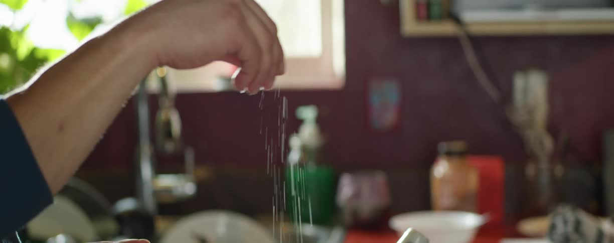 Person sprinkles seasoning in kitchen
