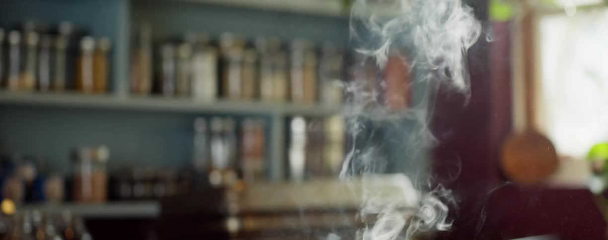 Smoke rises from steaks past shelves full of spices in kitchen