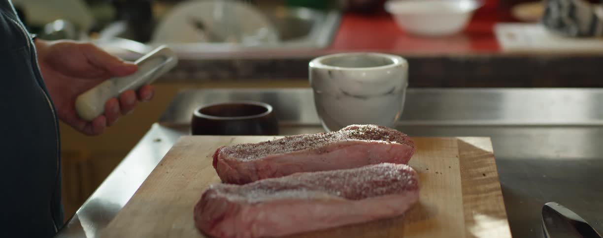 Person seasons thick steaks sitting on wooden board in kitchen