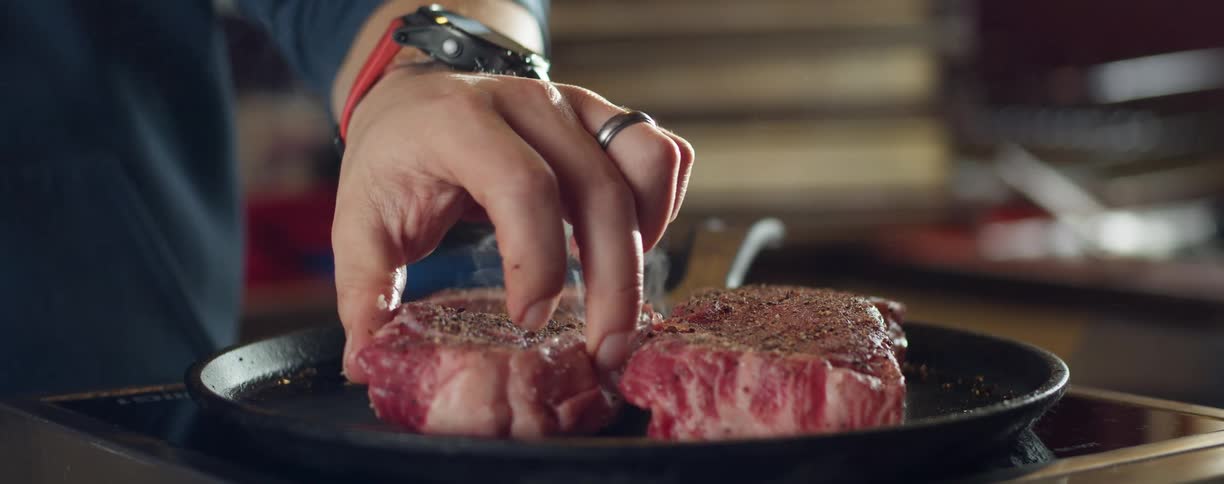 A man at home puts steaks on to a pan