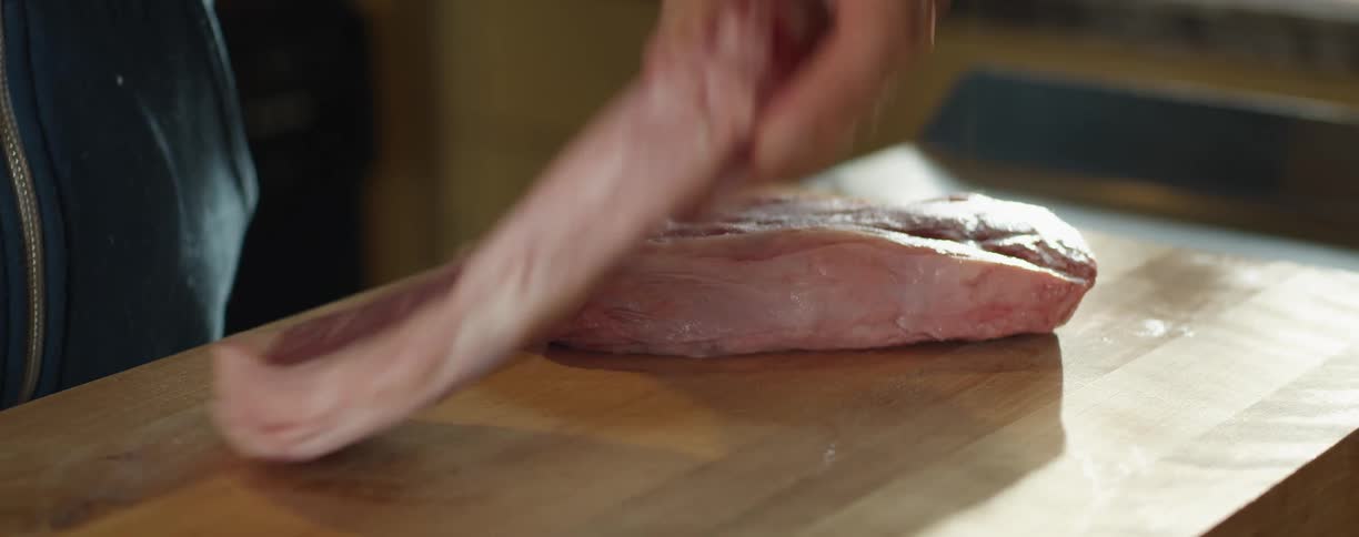 Man preparing two beef steaks over a wooden cutting board in the kitchen