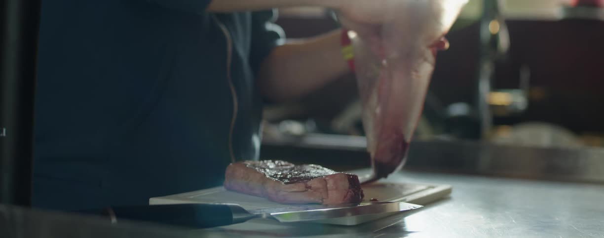 A person takes raw steaks from a plsatic bag in the kitchen of a restaurant
