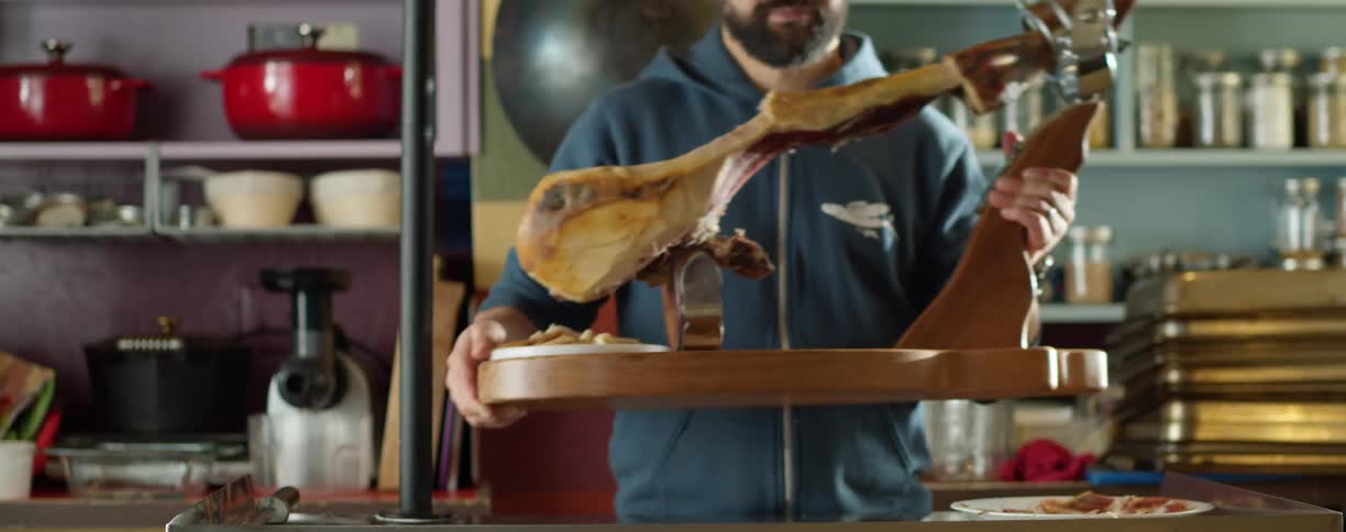 A person with a watch and hoodie placing a wooden tool on a counter with shelves and a wall in the background
