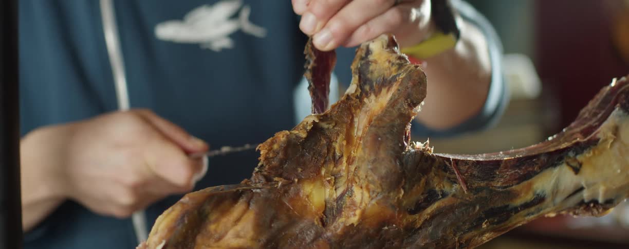 Person carves smaller pieces of meat from large cooked piece