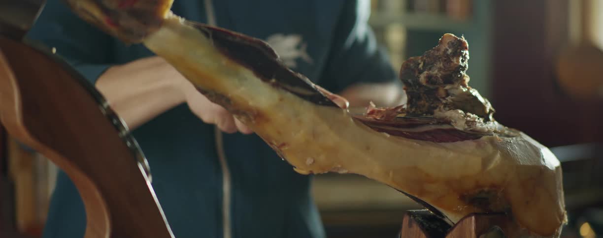 A man thinly slices meat from a cured pig leg
